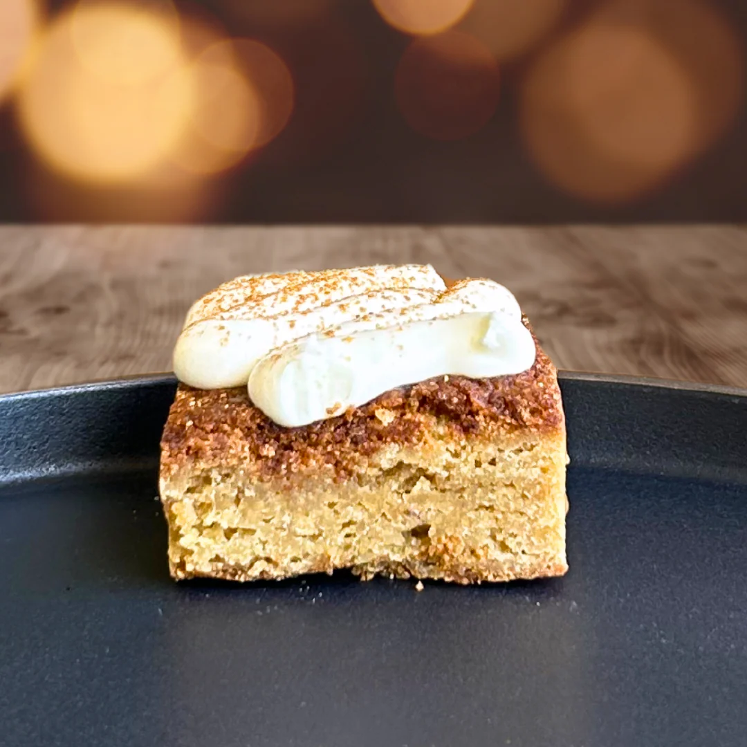 Cinnamon roll blondie topped with cream cheese frosting and cinnamon dust