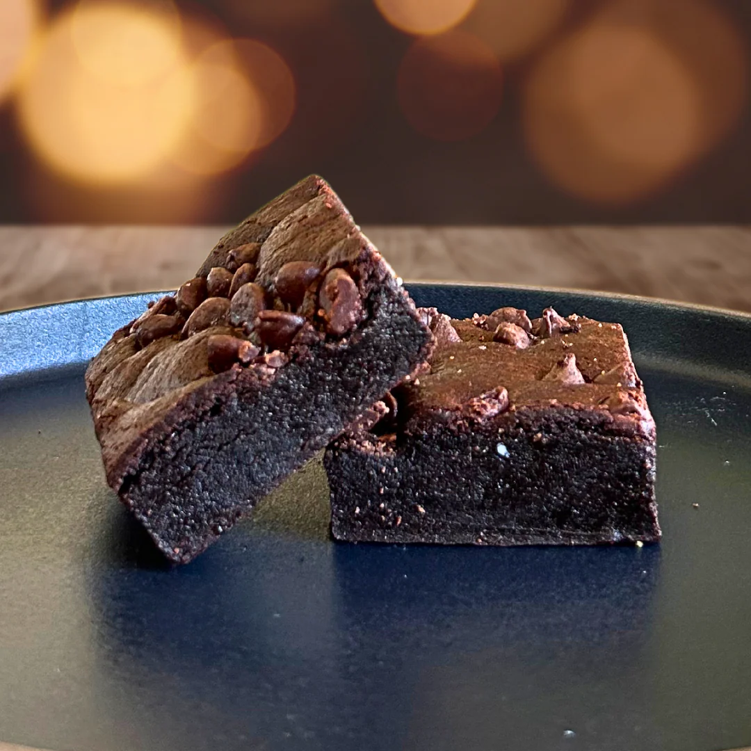Two Double Dark brownies stacked on a dark plate, tops studded with chocolate chips